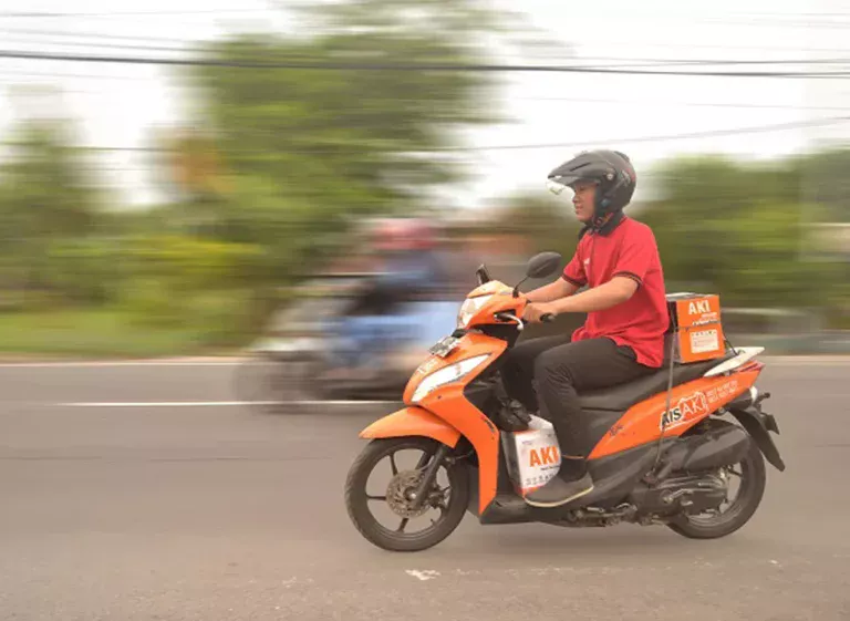seorang petugas yang mengantar aki dengan mengendarai motor berwarna oranye