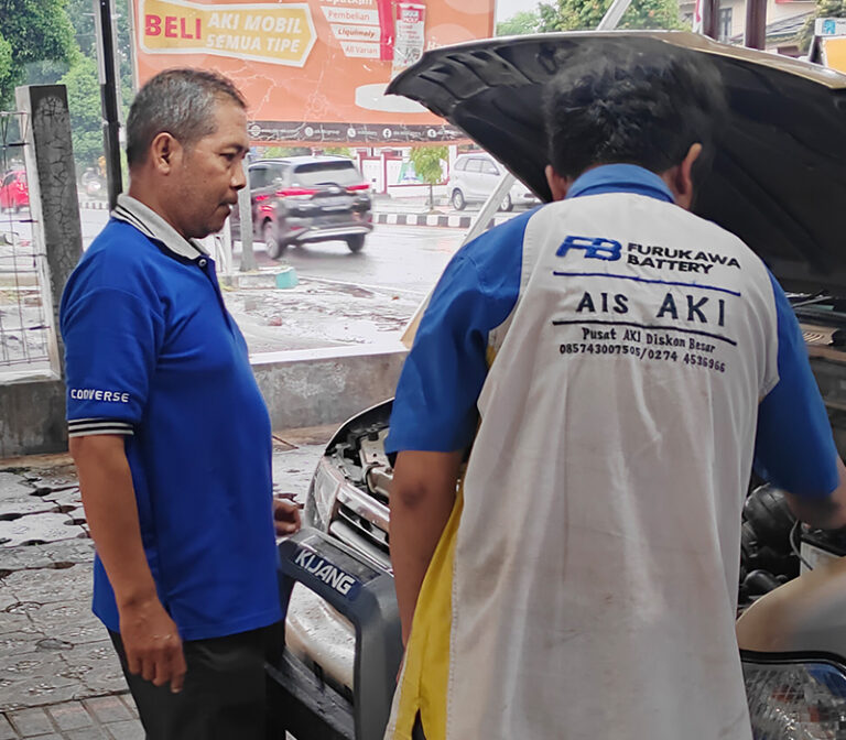 seorang pria sedang memperbaiki aki mobil pelanggan