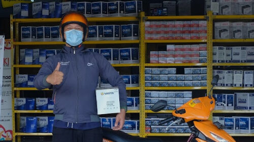 Seseorang sedang memgang aki dan di belakangnya ada toko aki.