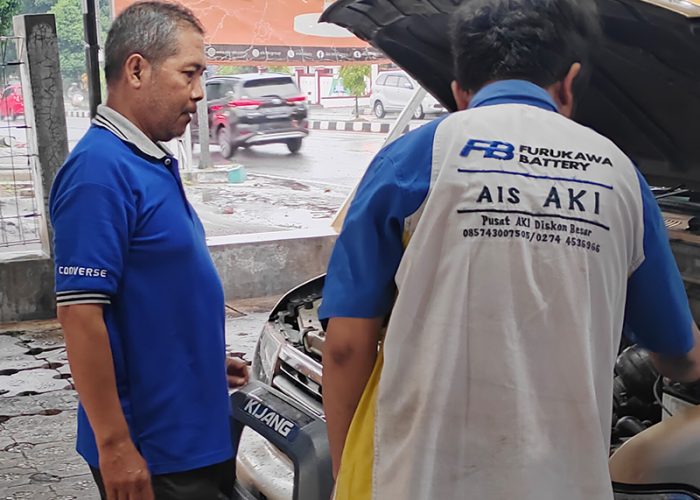 seorang pria sedang memperbaiki aki mobil pelanggan